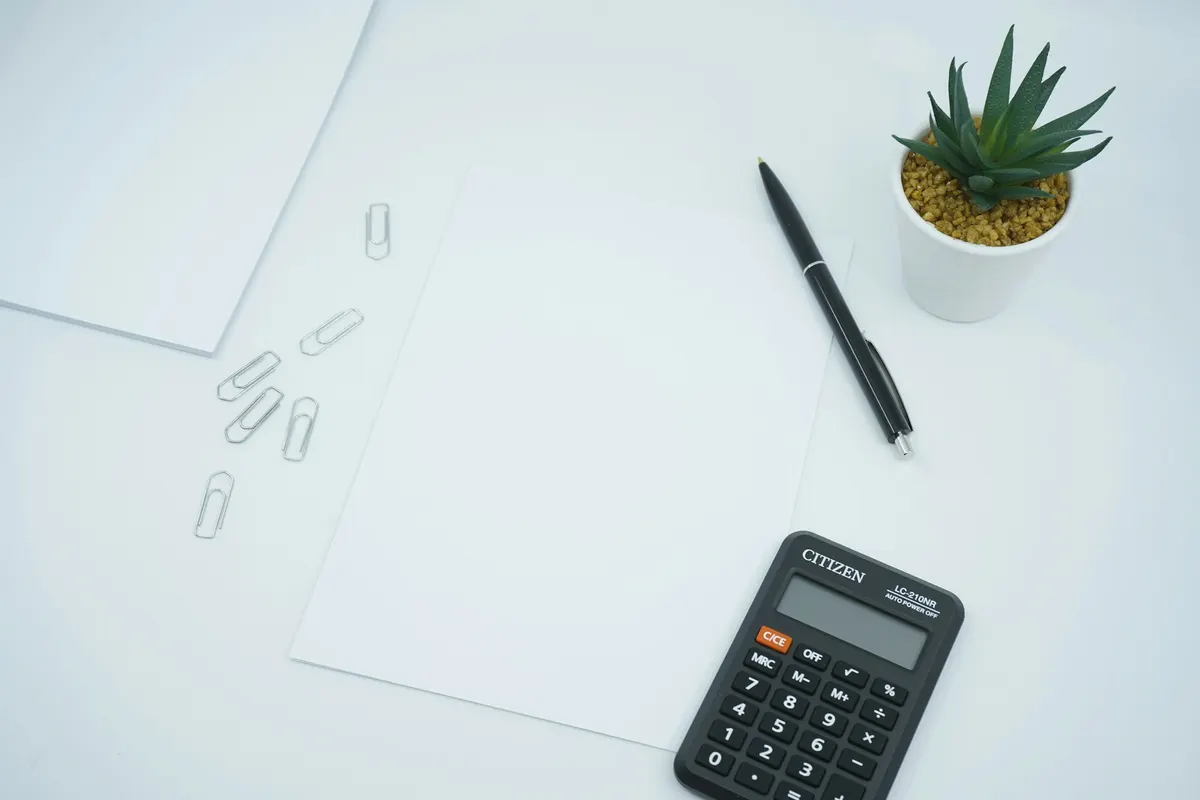 Feuilles blanches, stylo, trombones et calculatrice sur un bureau