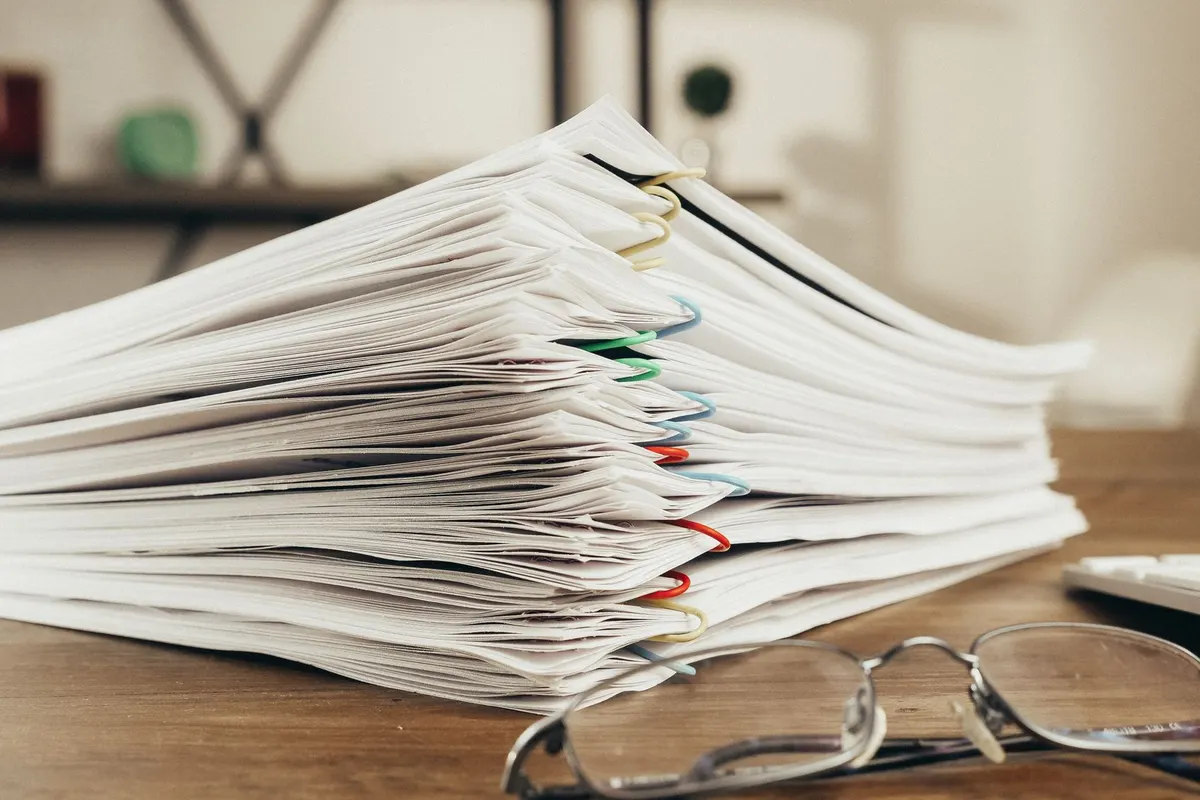 Pile de documents trombonés sur un bureau, avec des lunettes